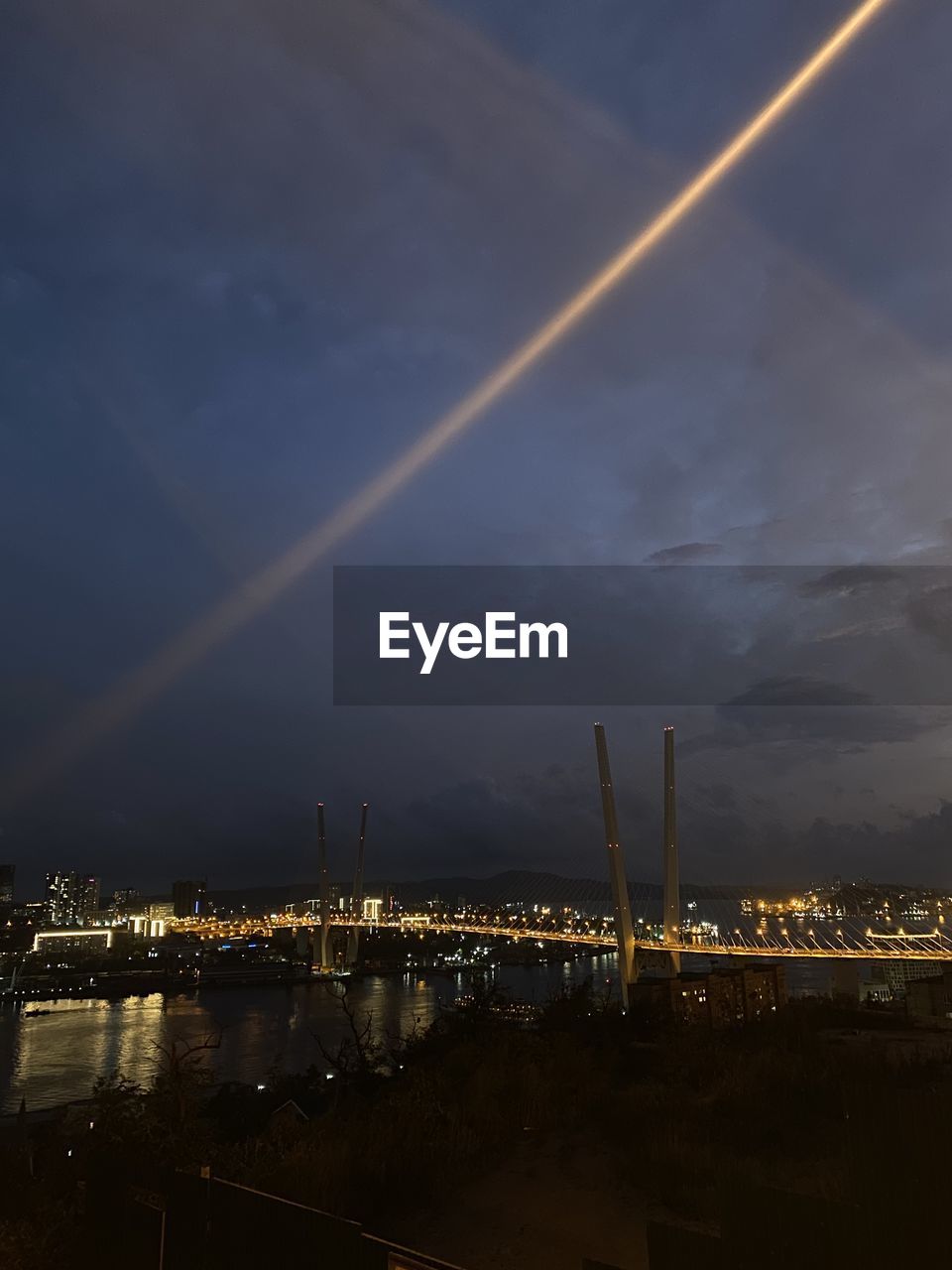 Illuminated city by river against sky at night