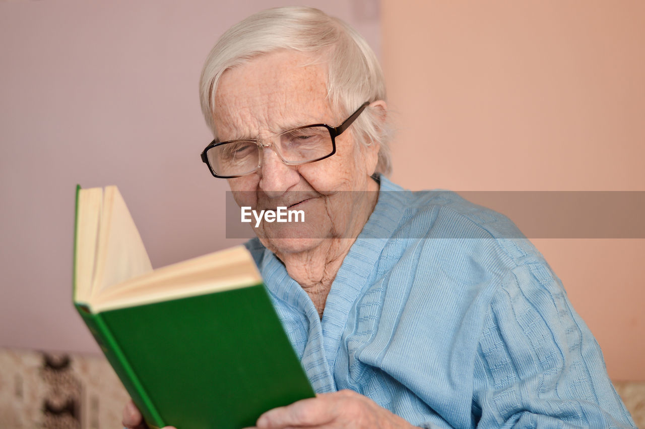 Old senior woman 90 years old holding open paper book in hands, reading best seller novel concept