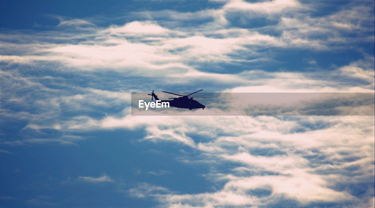 Side view of silhouette helicopter against clouds