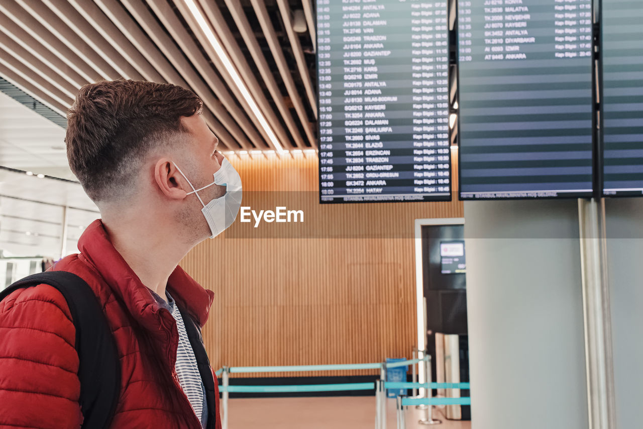Man wearing a mask protection at an airport. looking to the screen with departure information. 