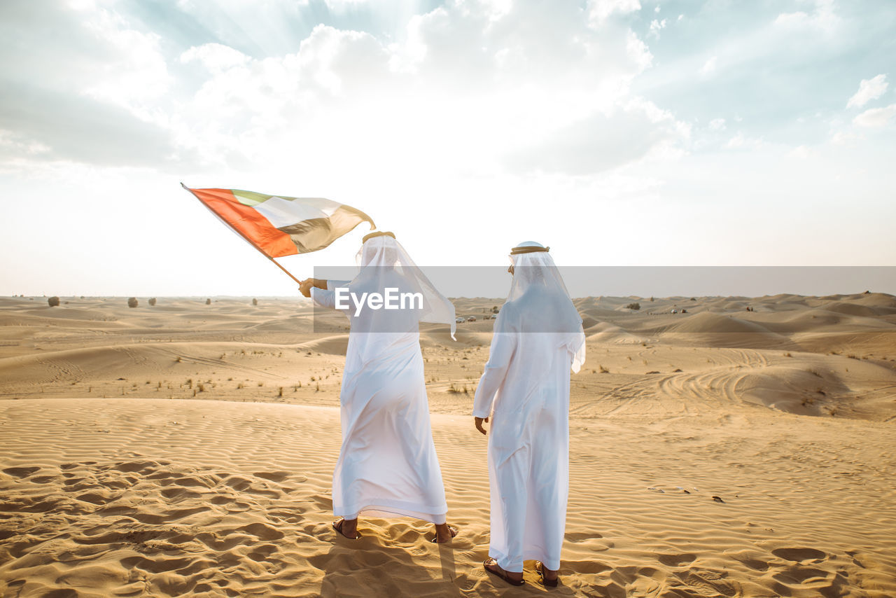 Man holding flag on sand dune against the sky