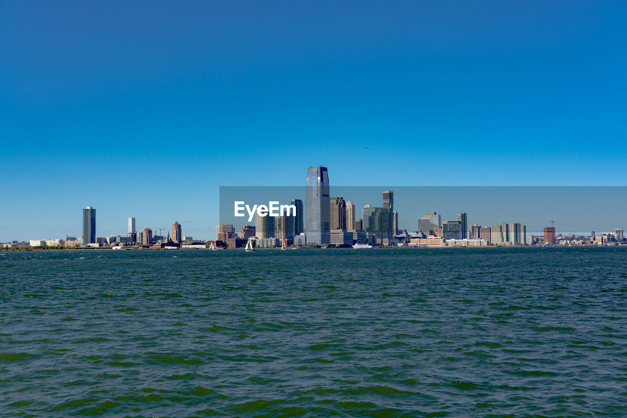 Scenic view of sea in front of cityscape against clear sky