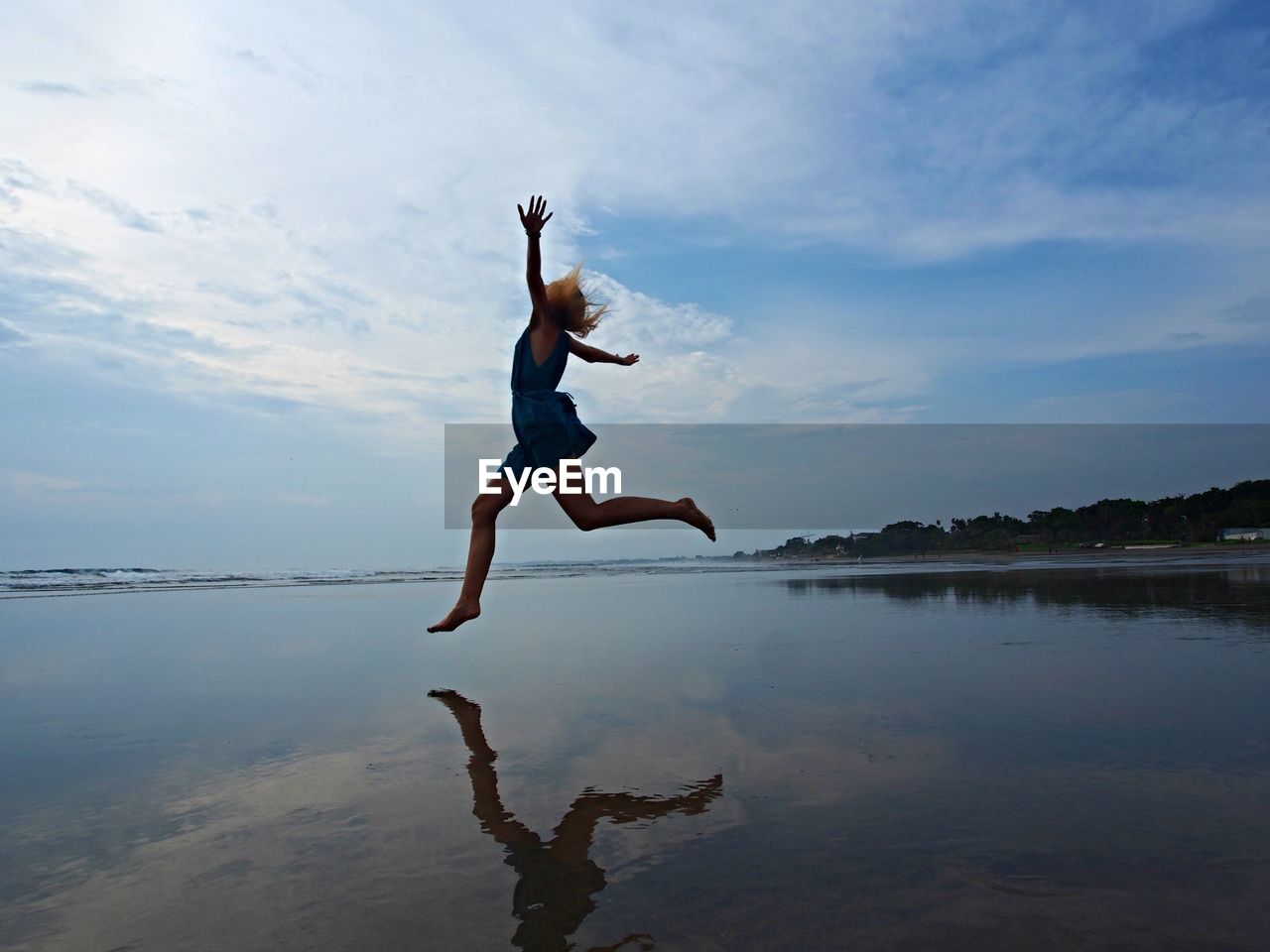 Full length of woman jumping at beach against sky