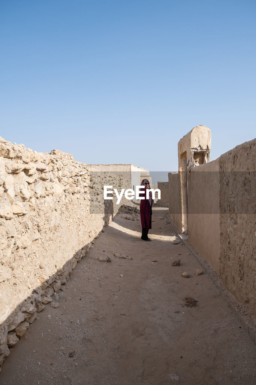 REAR VIEW OF WOMAN WALKING ON STREET AGAINST CLEAR SKY