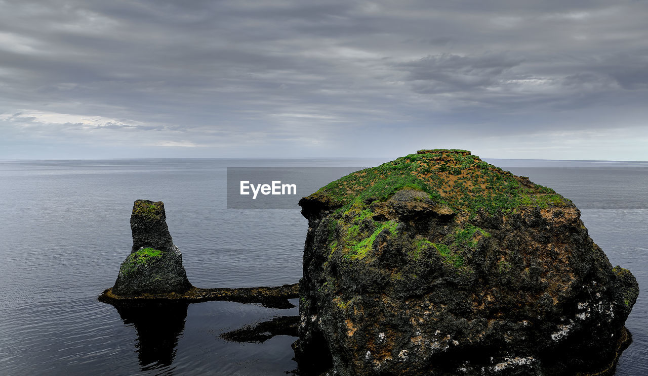 Scenic view of rocks by sea against sky