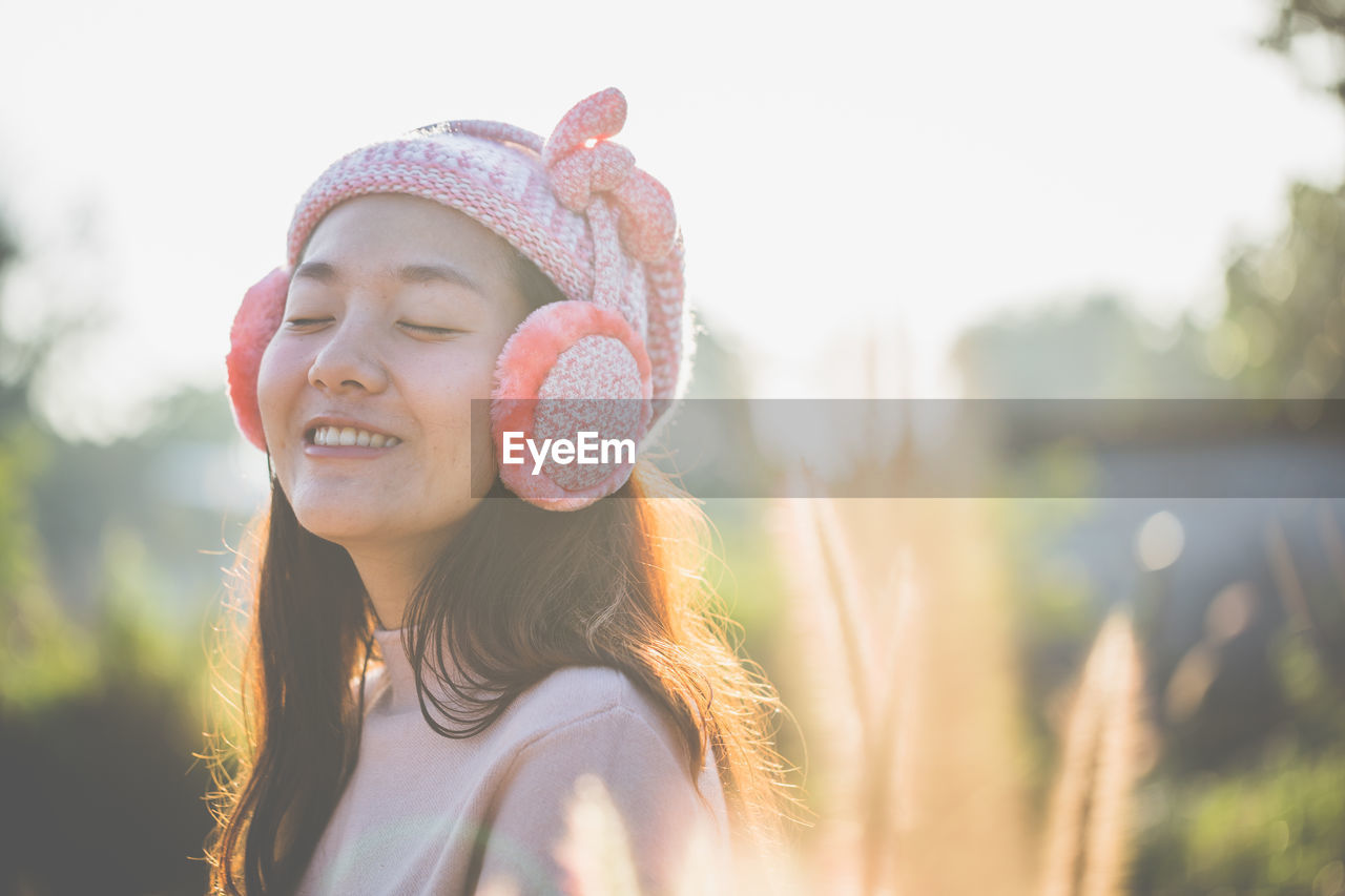 Smiling woman wearing hat and ear muffs during sunny day