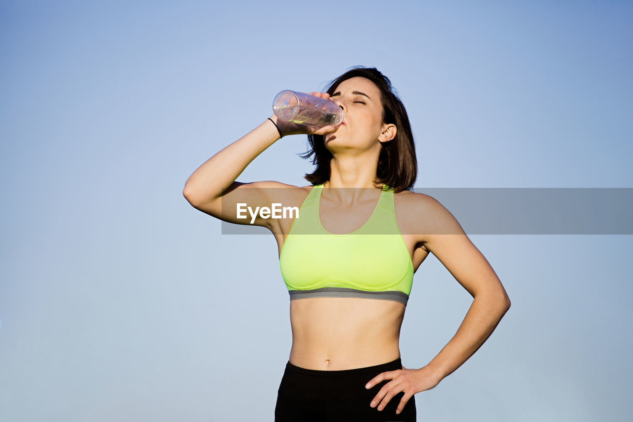 Woman drinking water while standing against clear sky
