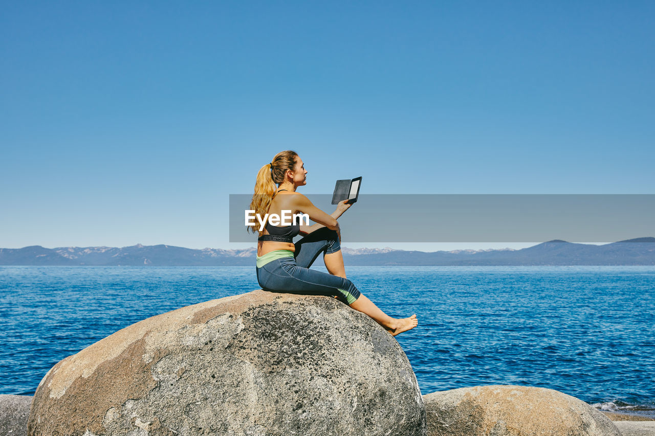 Young woman sitting by lake tahoe reading a kindle book during the day