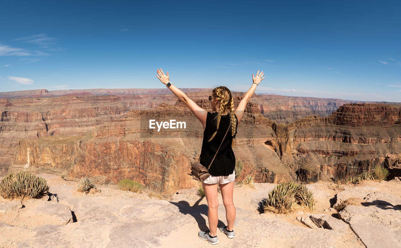 Rear view of woman standing on rock against sky