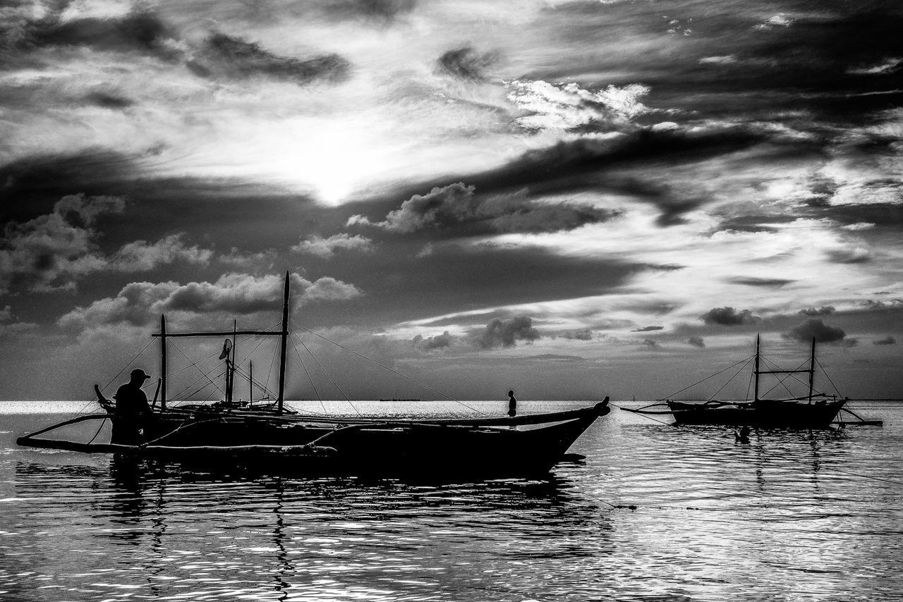 Silhouette fisherman on outrigger boat at sea against cloudy sky