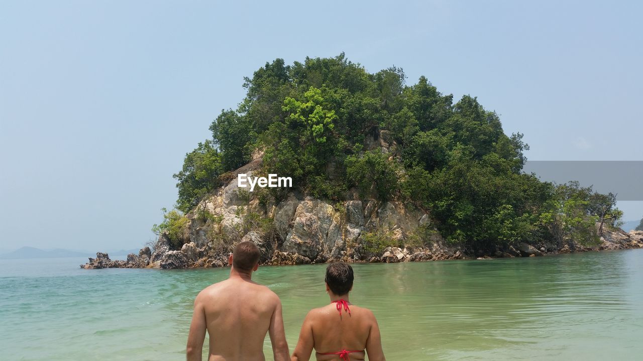 Rear view of couple by sea against rock formation