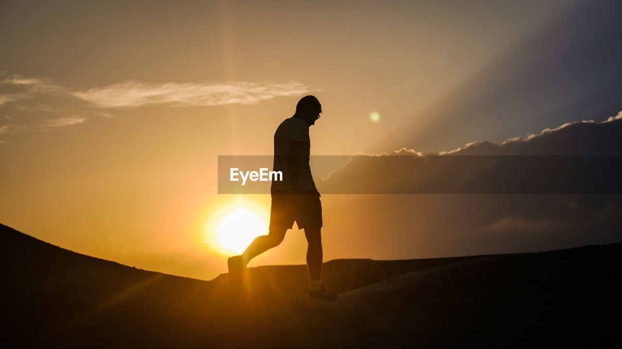 SILHOUETTE MAN STANDING ON MOUNTAIN AGAINST BRIGHT SUN