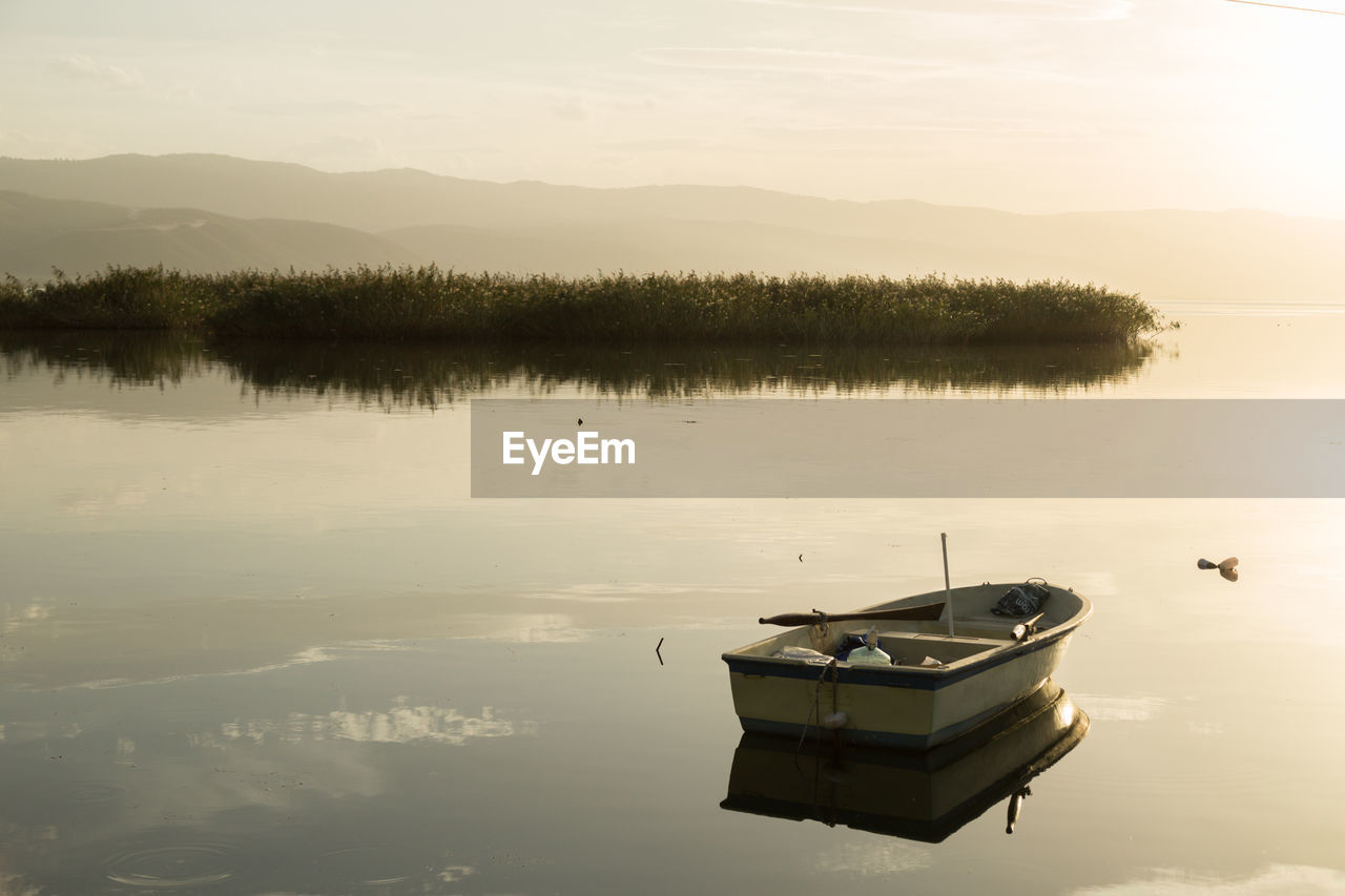 Boat moored in lake against sky during sunset