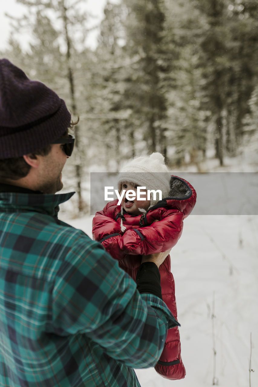 Side view of father carrying cute daughter while standing in forest during winter