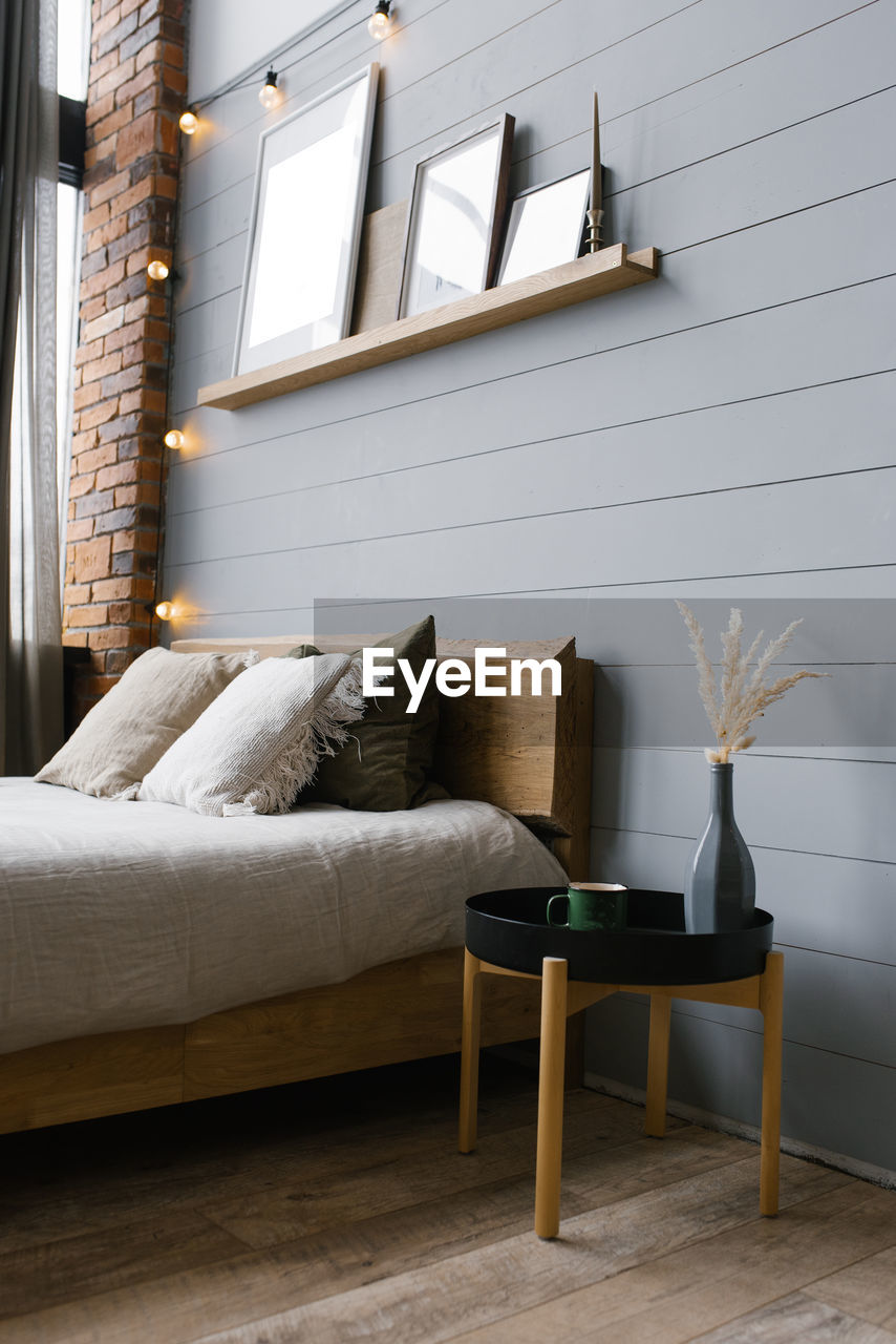 A modern white ceramic vase with dried grass and a cup of coffee or tea beside the double bed.