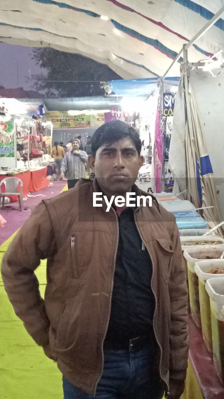 PORTRAIT OF YOUNG MAN STANDING AT MARKET STALL