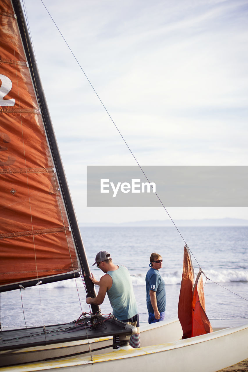 Man making sailboat while standing with father at beach