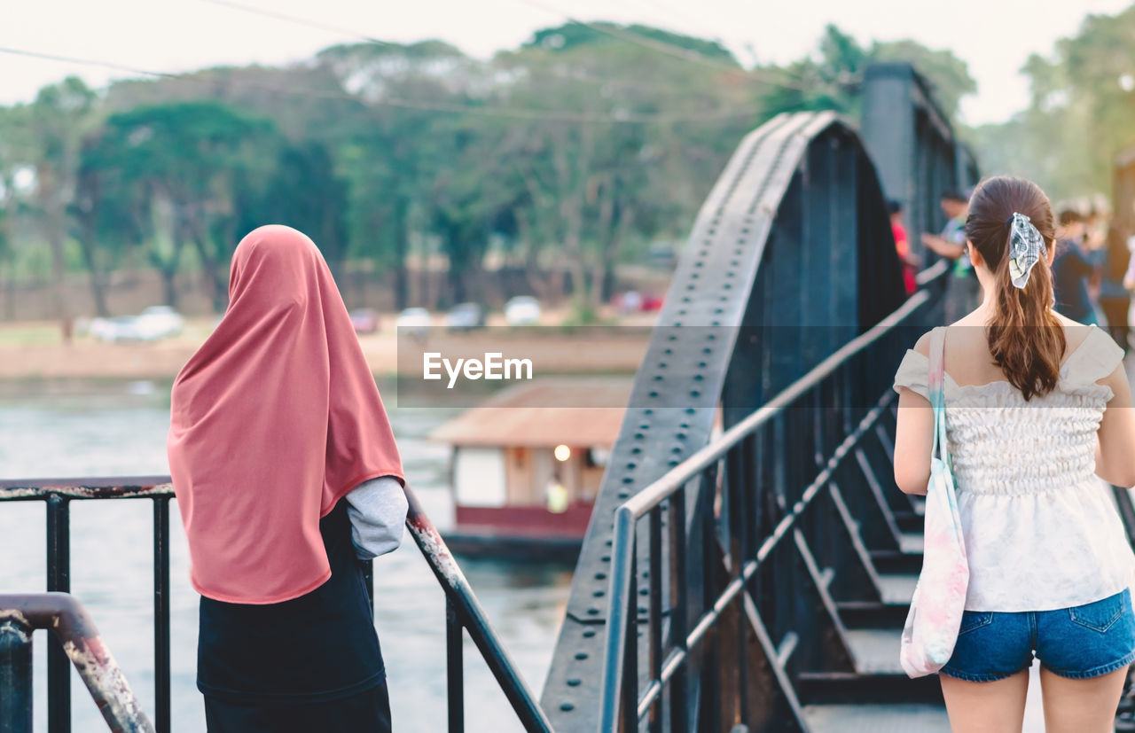 REAR VIEW OF WOMEN STANDING BY RAILING