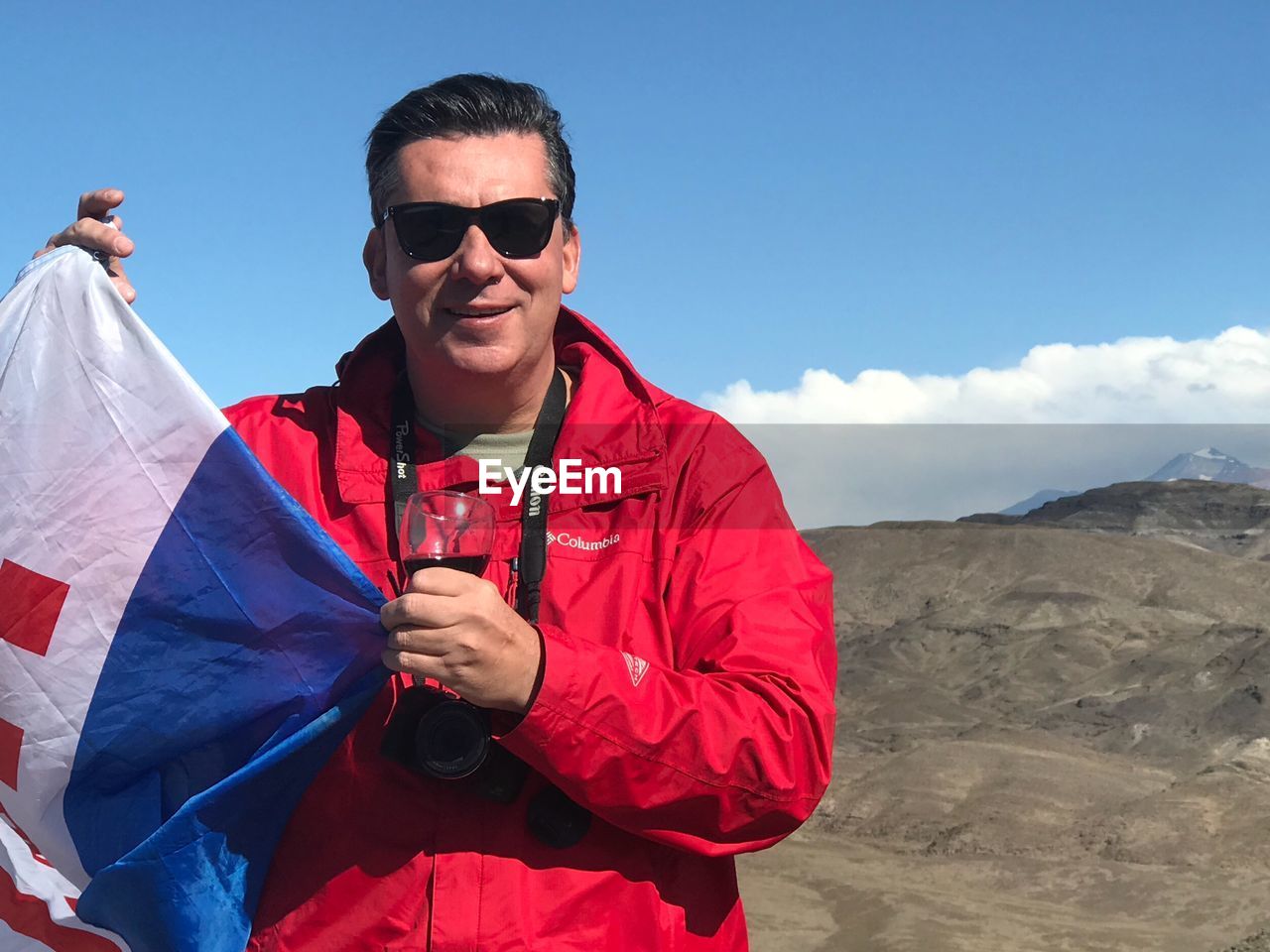 Portrait of man in sunglasses holding flag against sky