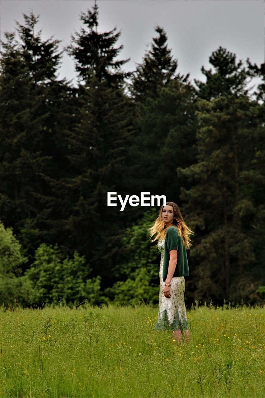 Young woman on grassy field against trees