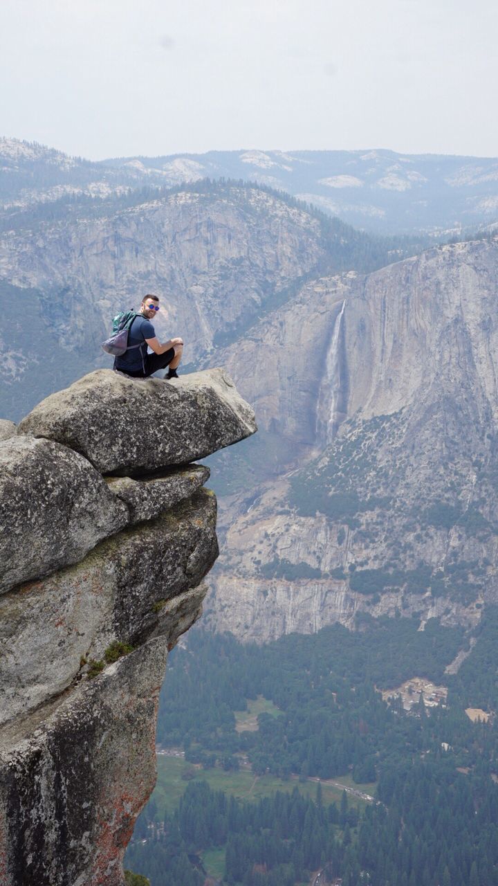 MAN ON CLIFF AGAINST MOUNTAIN