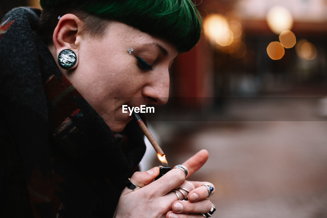 Portrait of non-binary hipster woman lighting a cigarette in city