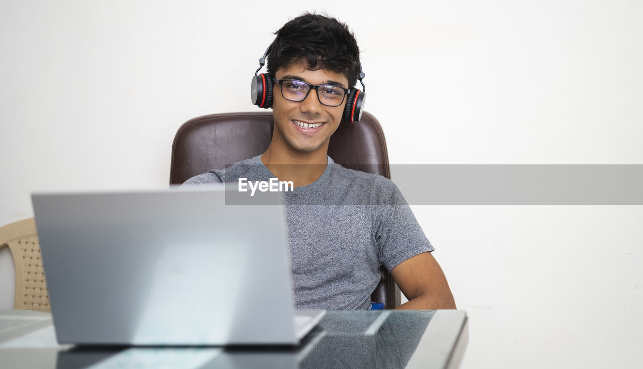 PORTRAIT OF SMILING YOUNG MAN USING LAPTOP