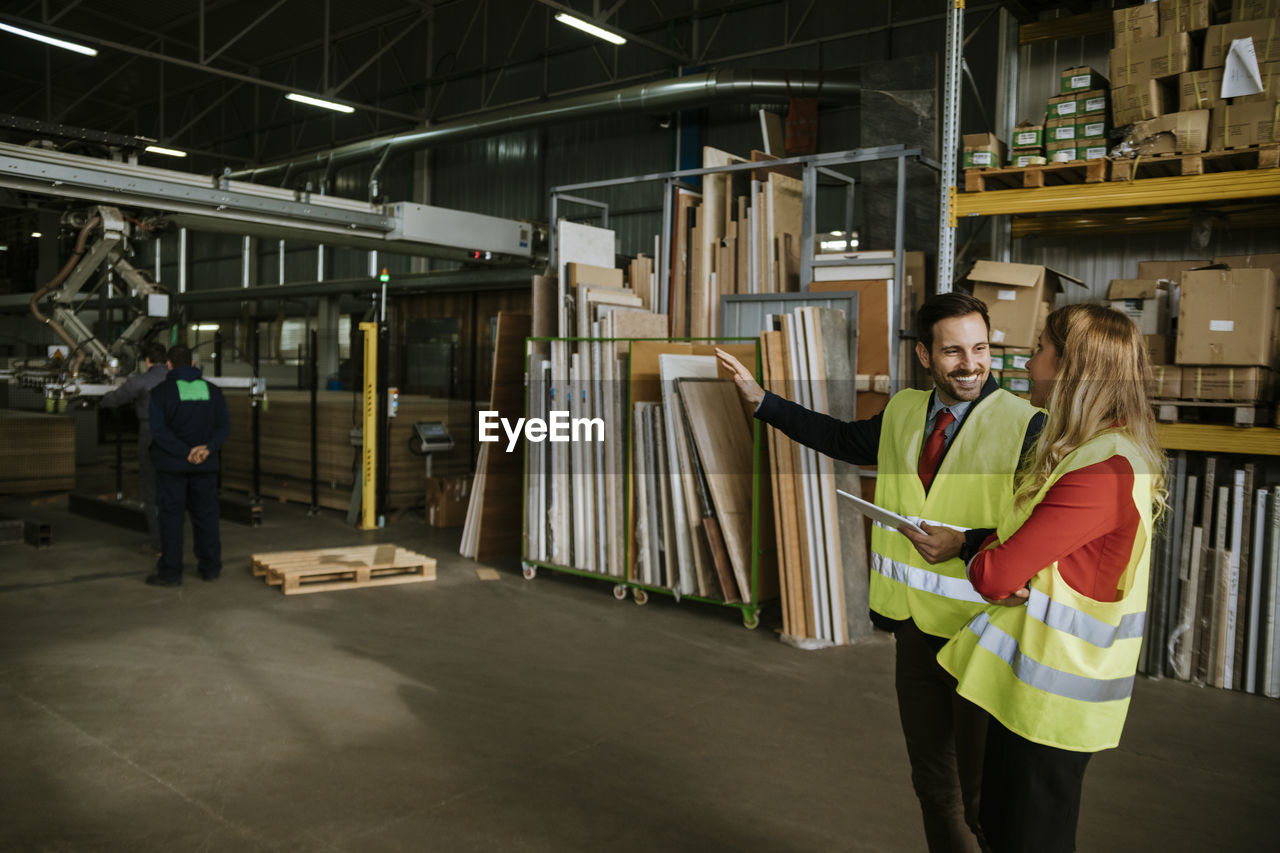 Smiling man and woman wearing reflective vests in warehouse