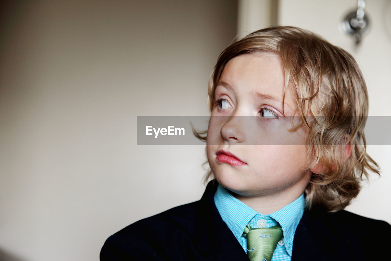 Close-up of boy wearing suit looking away and standing at home