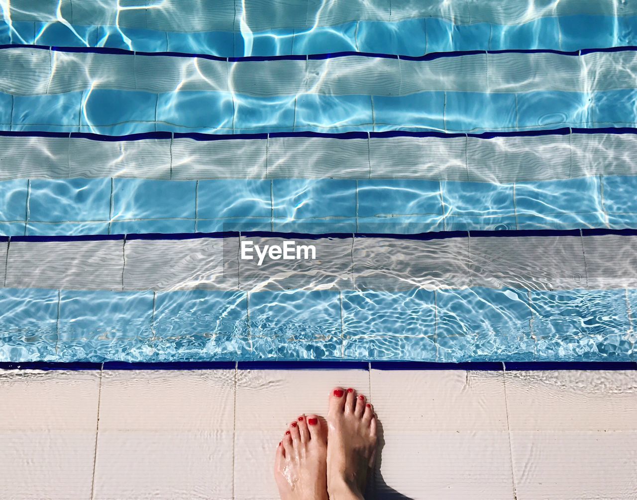 Low section of woman standing at poolside during sunny day