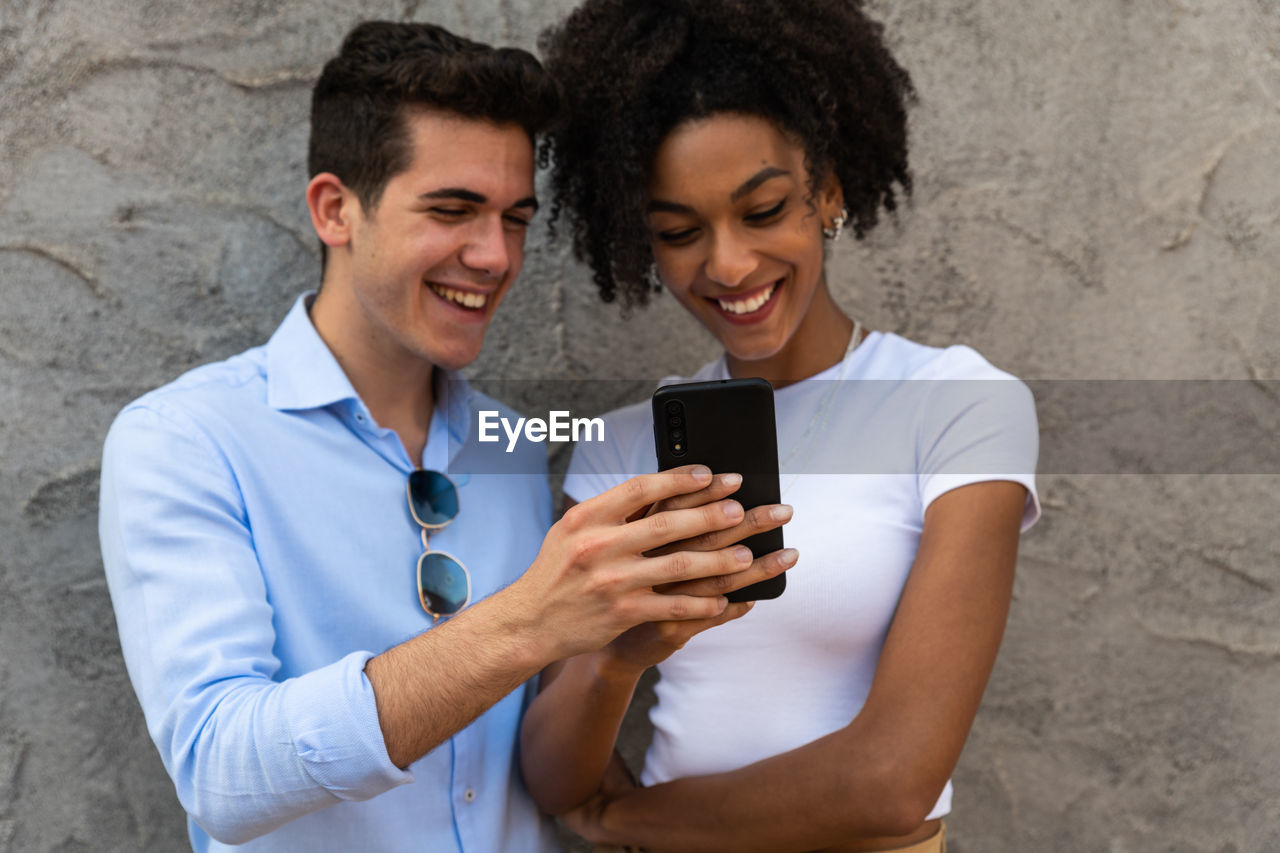 Smiling young couple embracing while looking at smartphone. multiethnic couple sharing social media