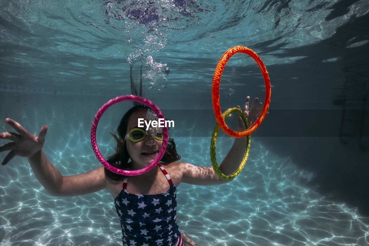 Smiling girl wearing swimming goggles while playing with colorful rings in pool