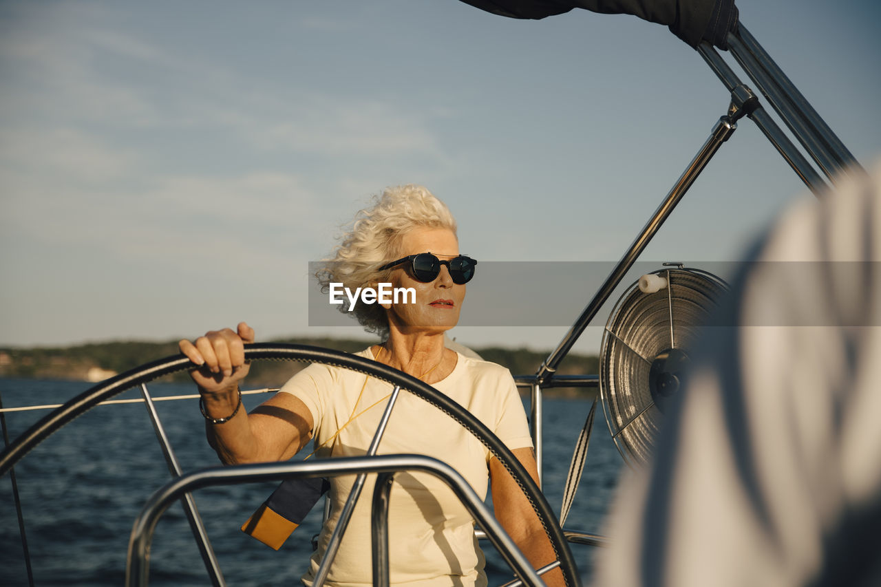 Senior woman looking away while sailing boat against sky on sunny day