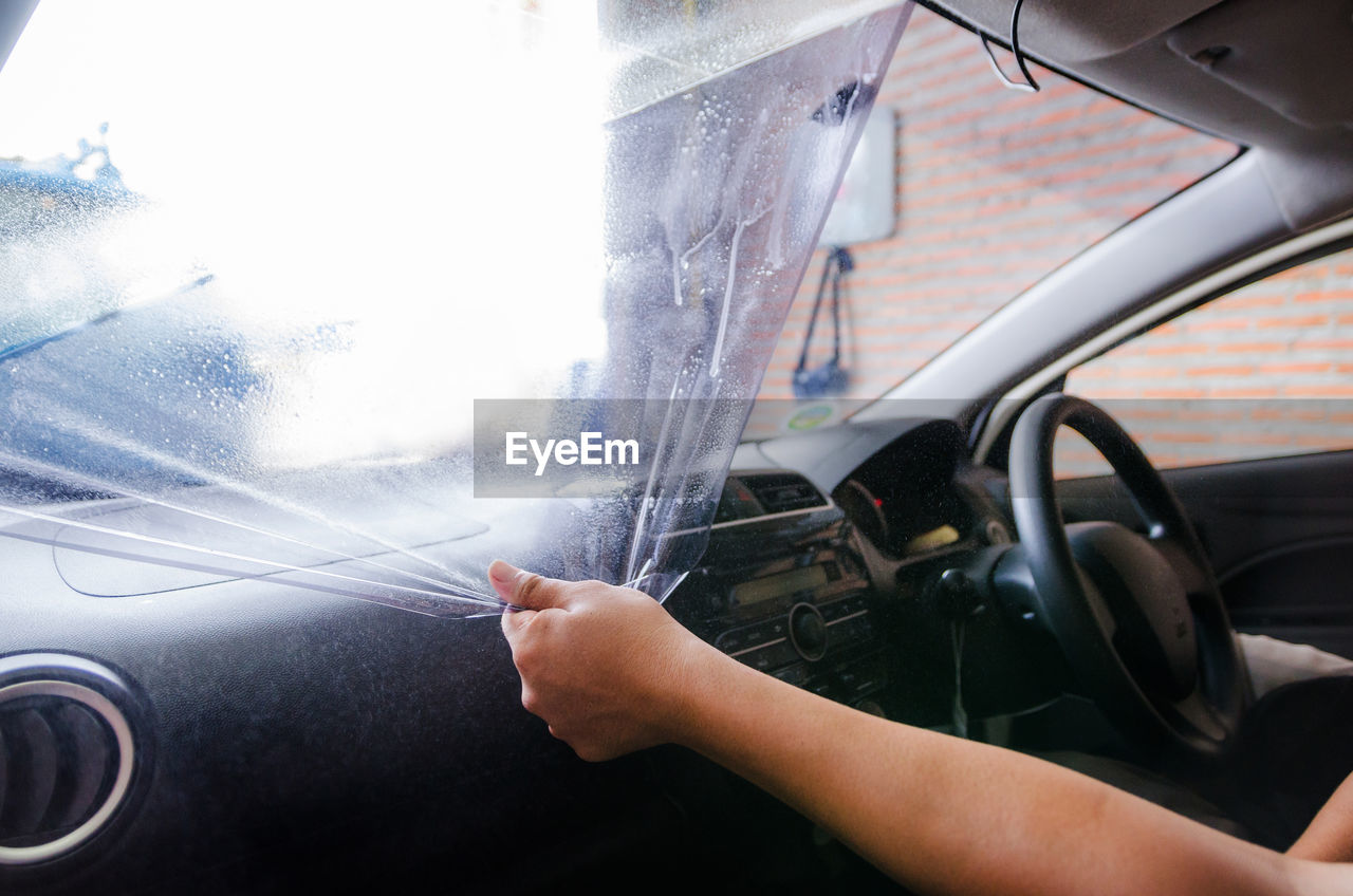 Cropped hands of woman removing plastic from car windshield