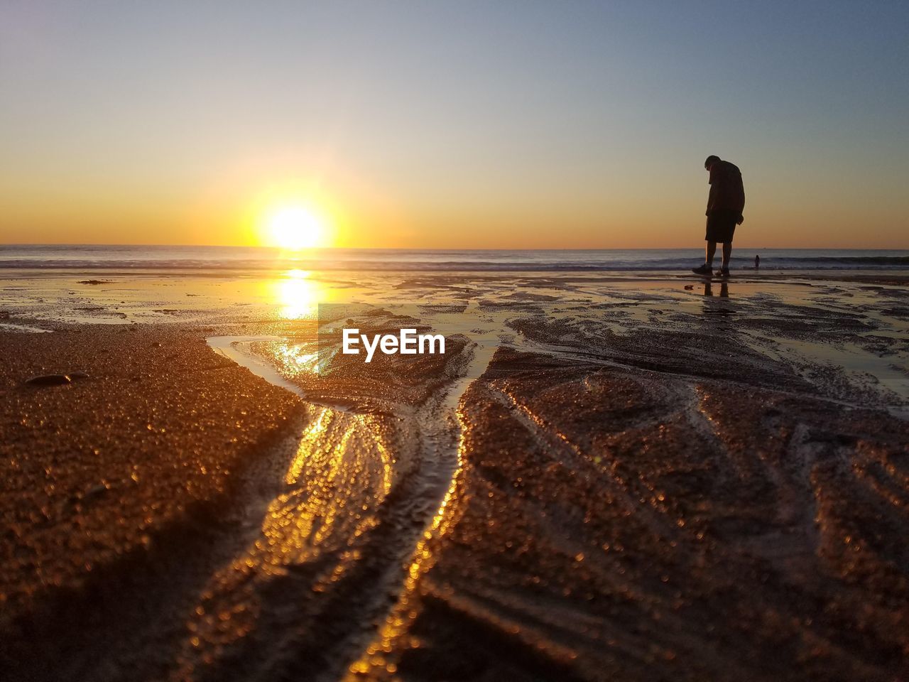 WOMAN STANDING ON BEACH DURING SUNSET