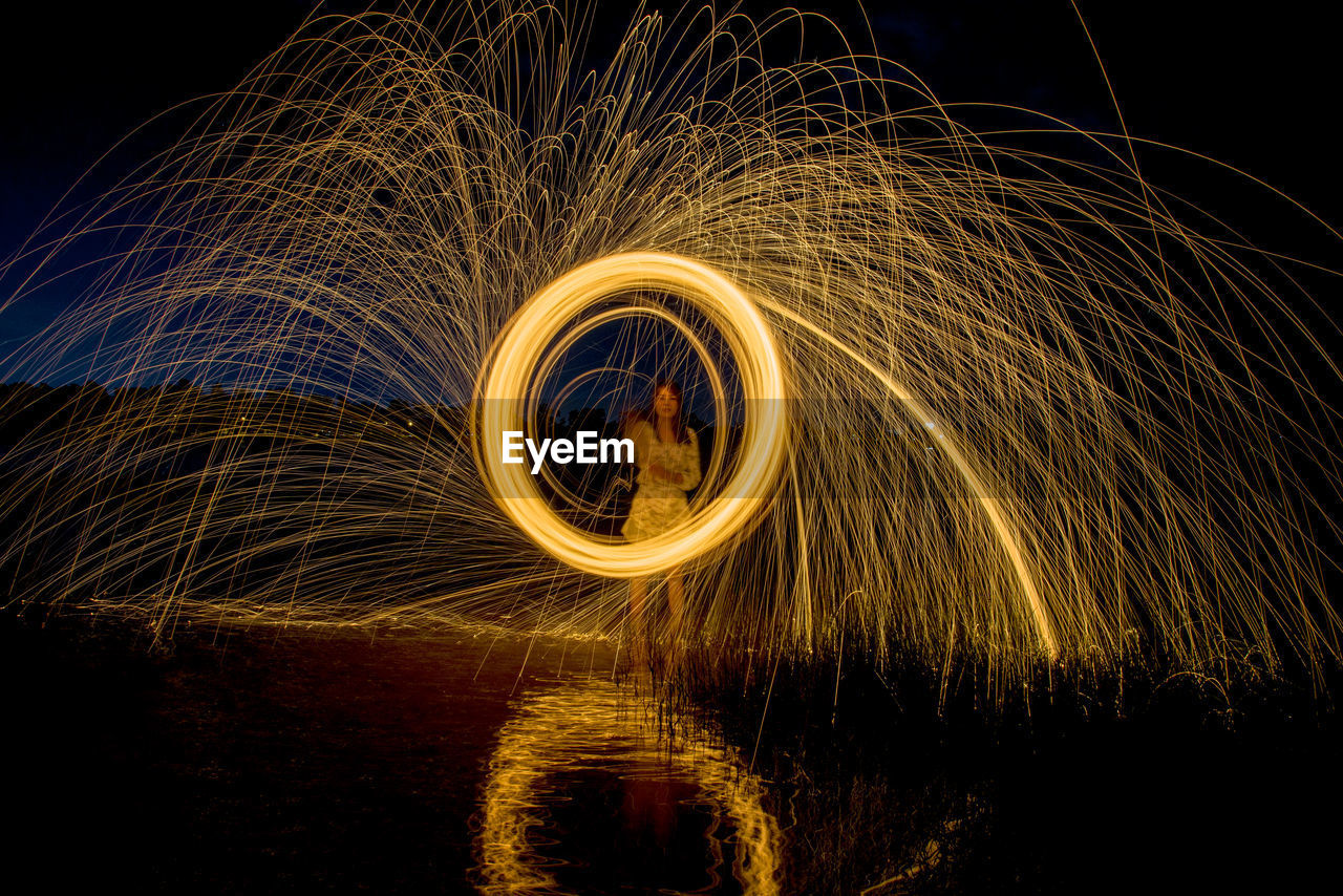 Burning steel wool spinning, trajectories of burning sparks on the surface of water lake by women