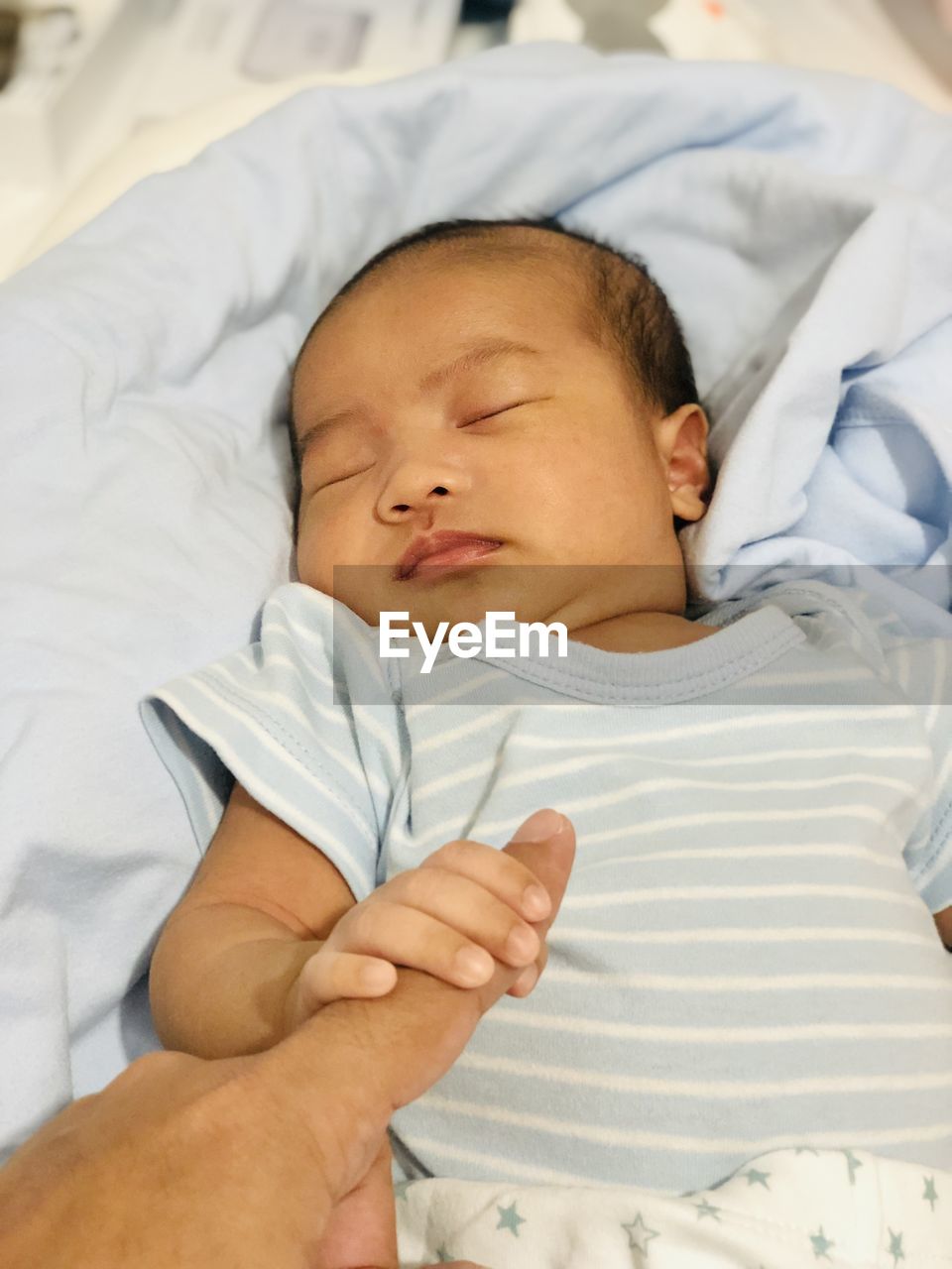 High angle view of baby boy sleeping on bed at home holding a finger