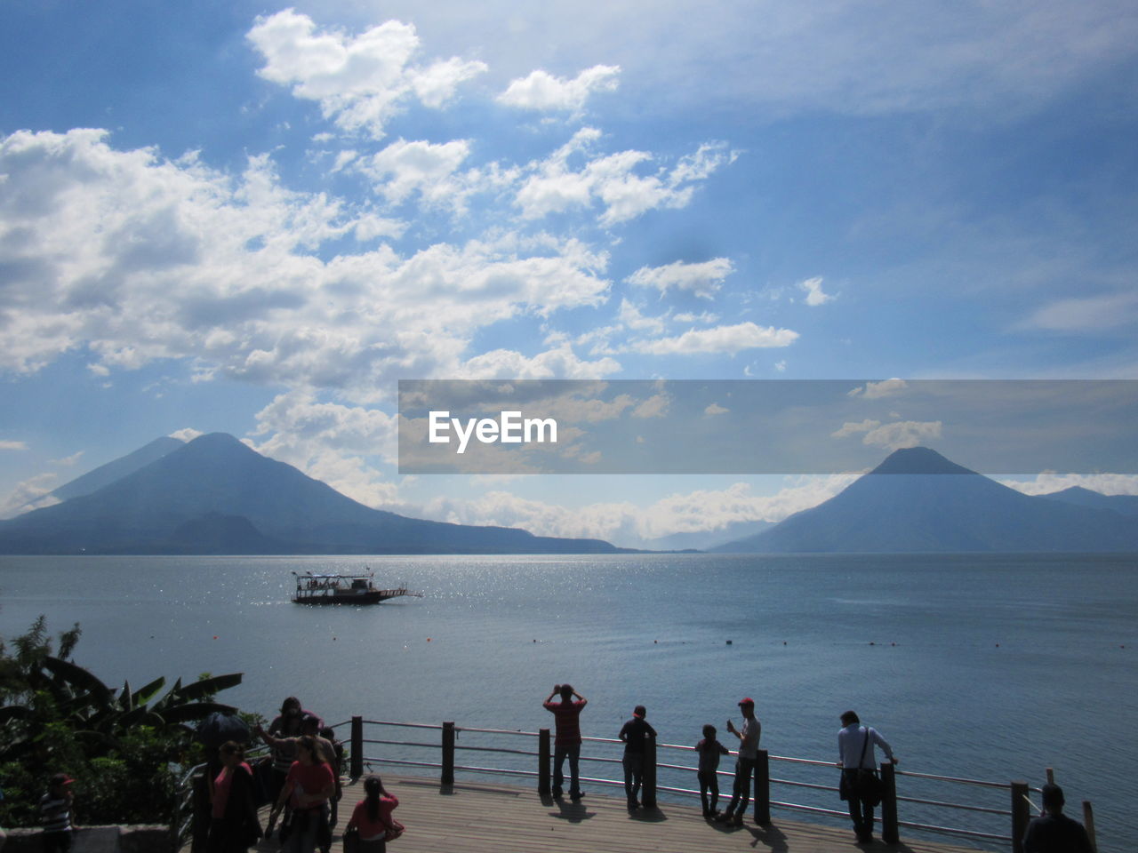 GROUP OF PEOPLE ON SEA SHORE AGAINST MOUNTAINS