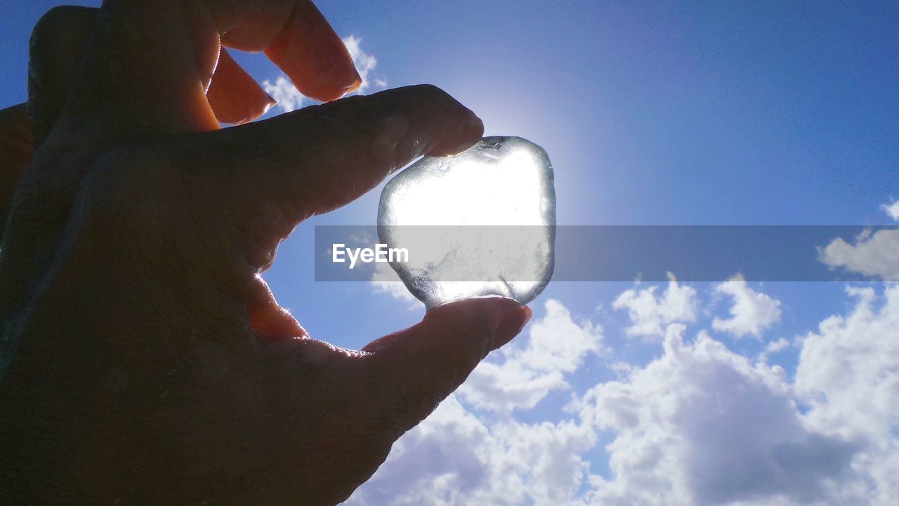 Cropped hand of person holding ice cube against sky