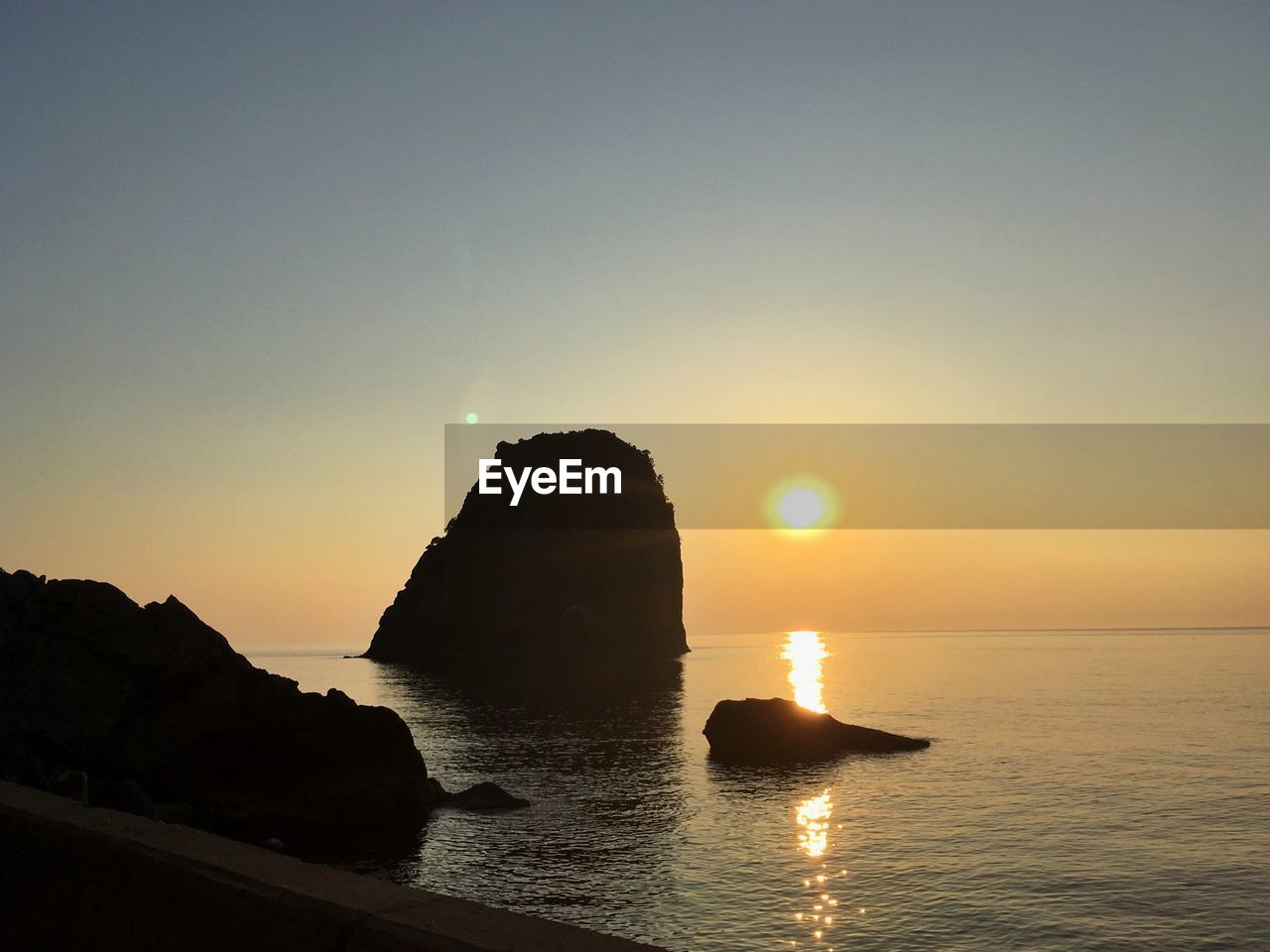 SILHOUETTE ROCKS BY SEA AGAINST SKY DURING SUNSET