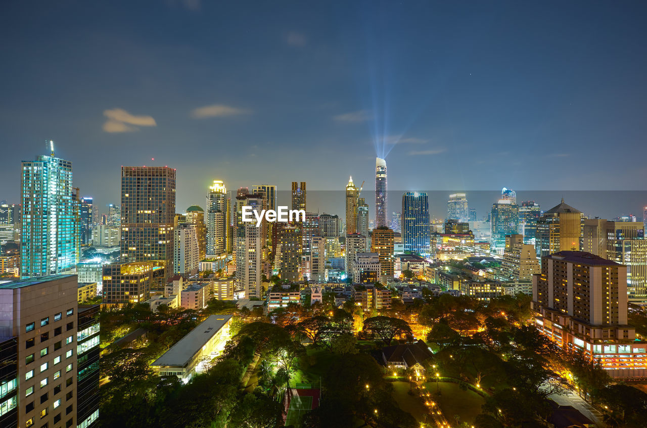 Illuminated modern buildings in city against sky at night