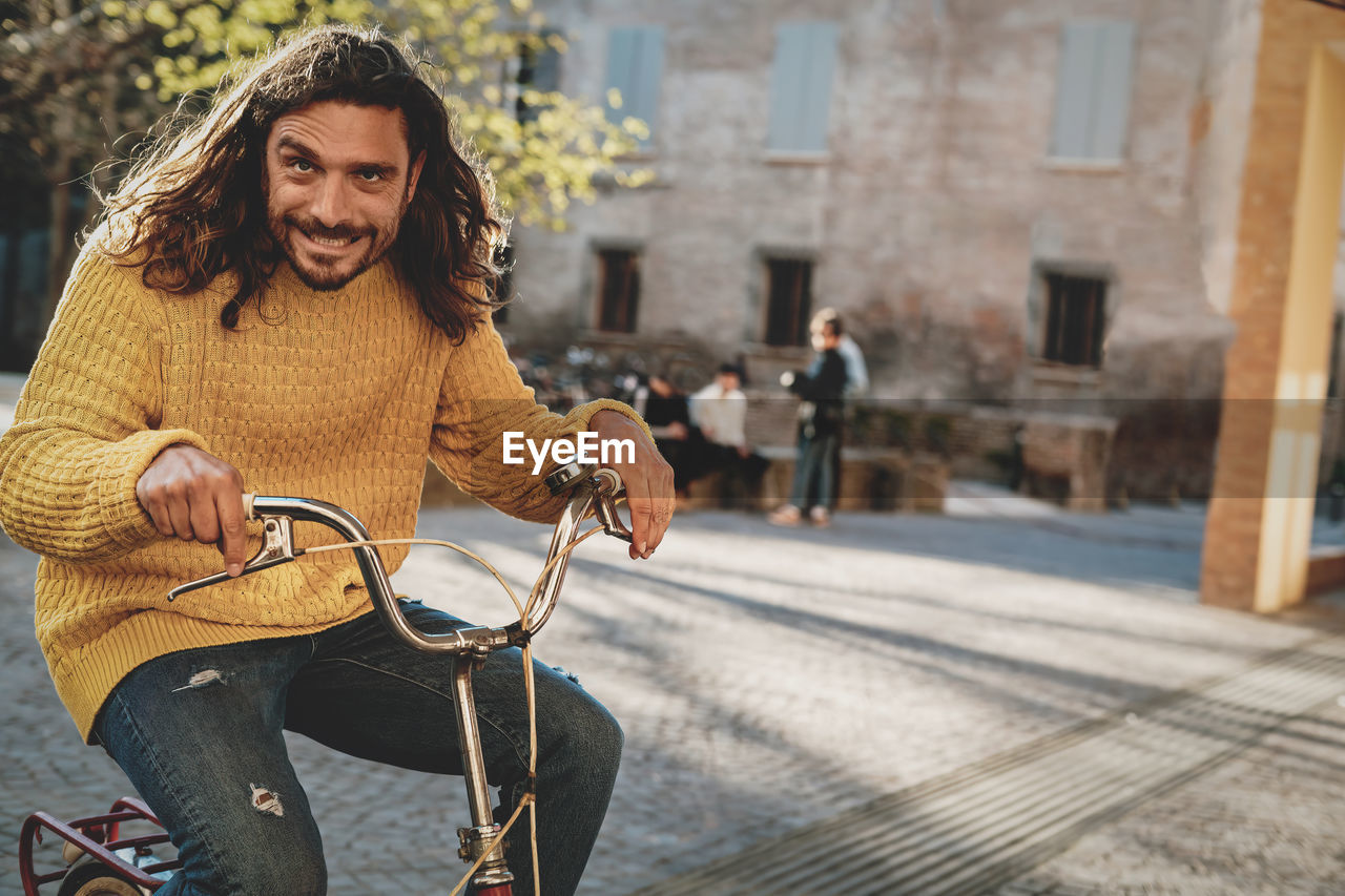 Funny long haired and bearded man taking a ride with a vintage bicycle in the street