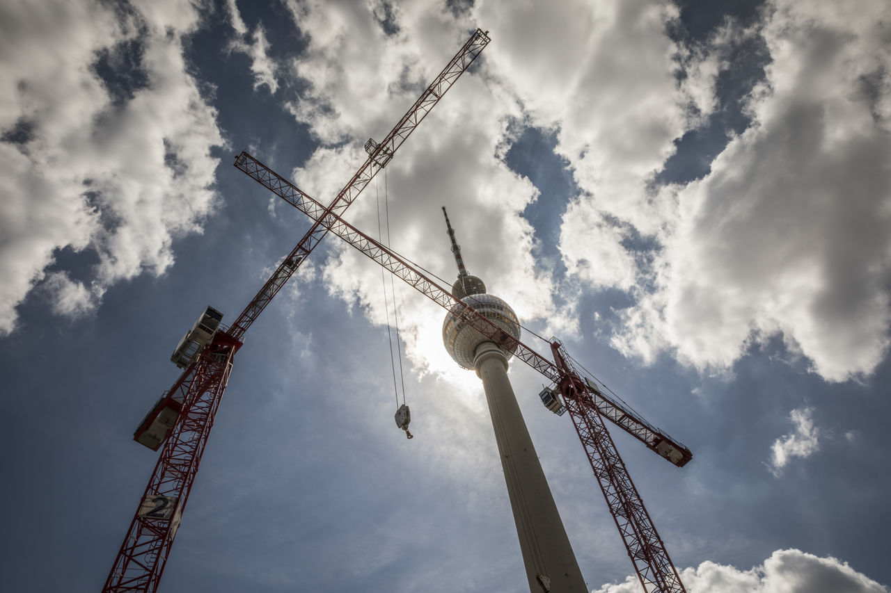 Cranes near berlin television tower under cloudy sky at alexanderplatz, berlin, germany