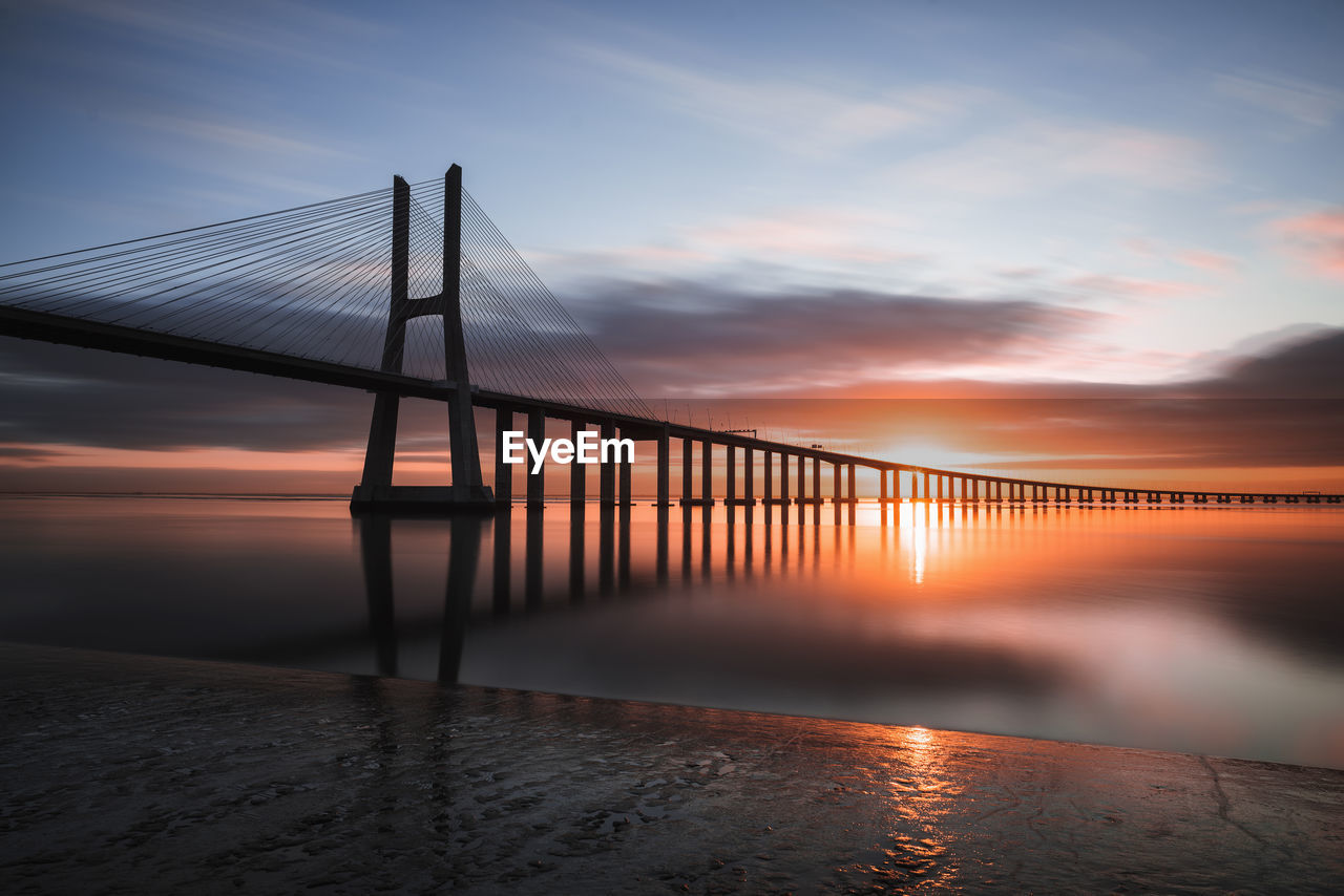 Silhouette bridge over sea against sky during sunset