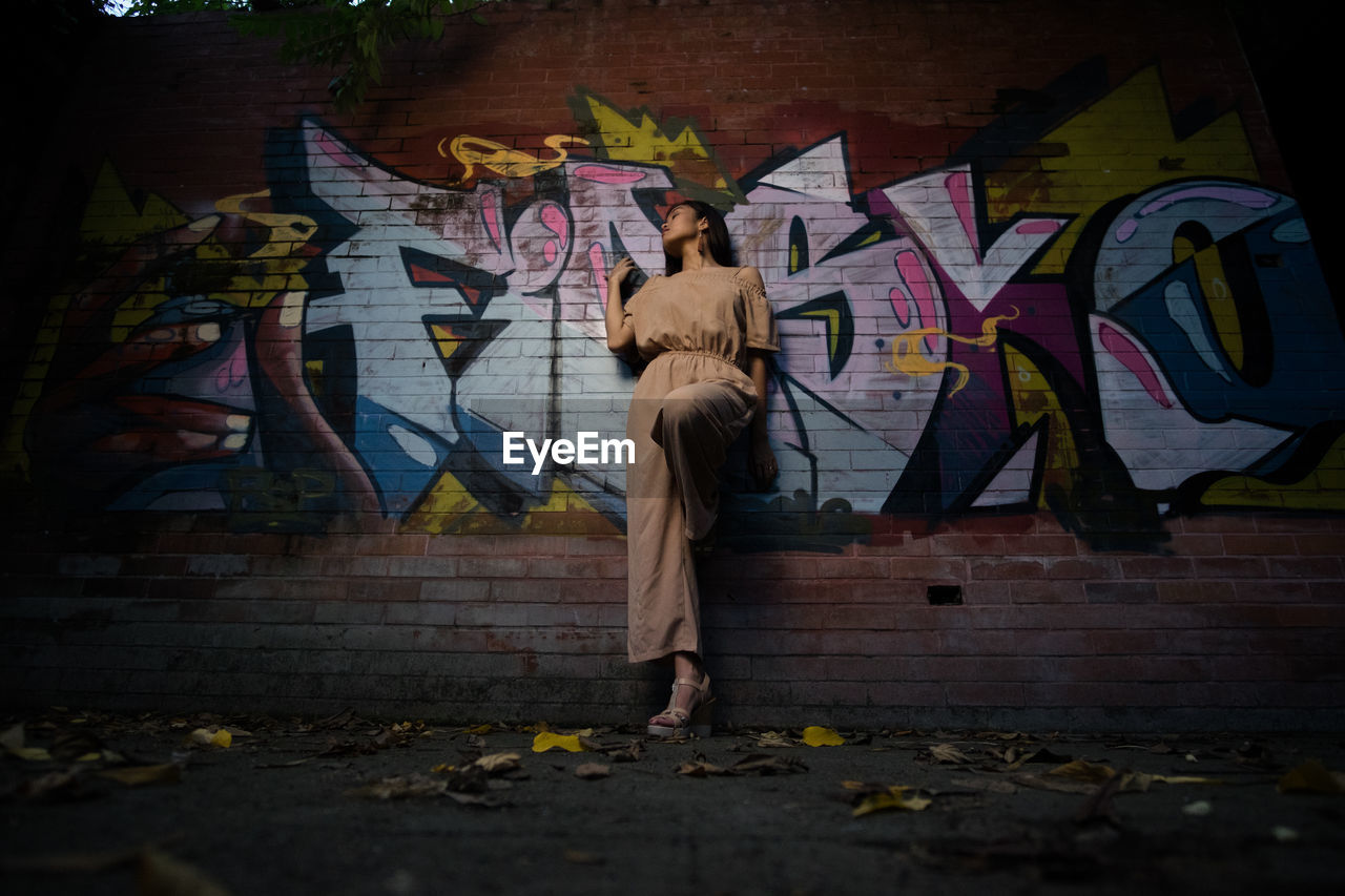 WOMAN STANDING ON GRAFFITI WALL