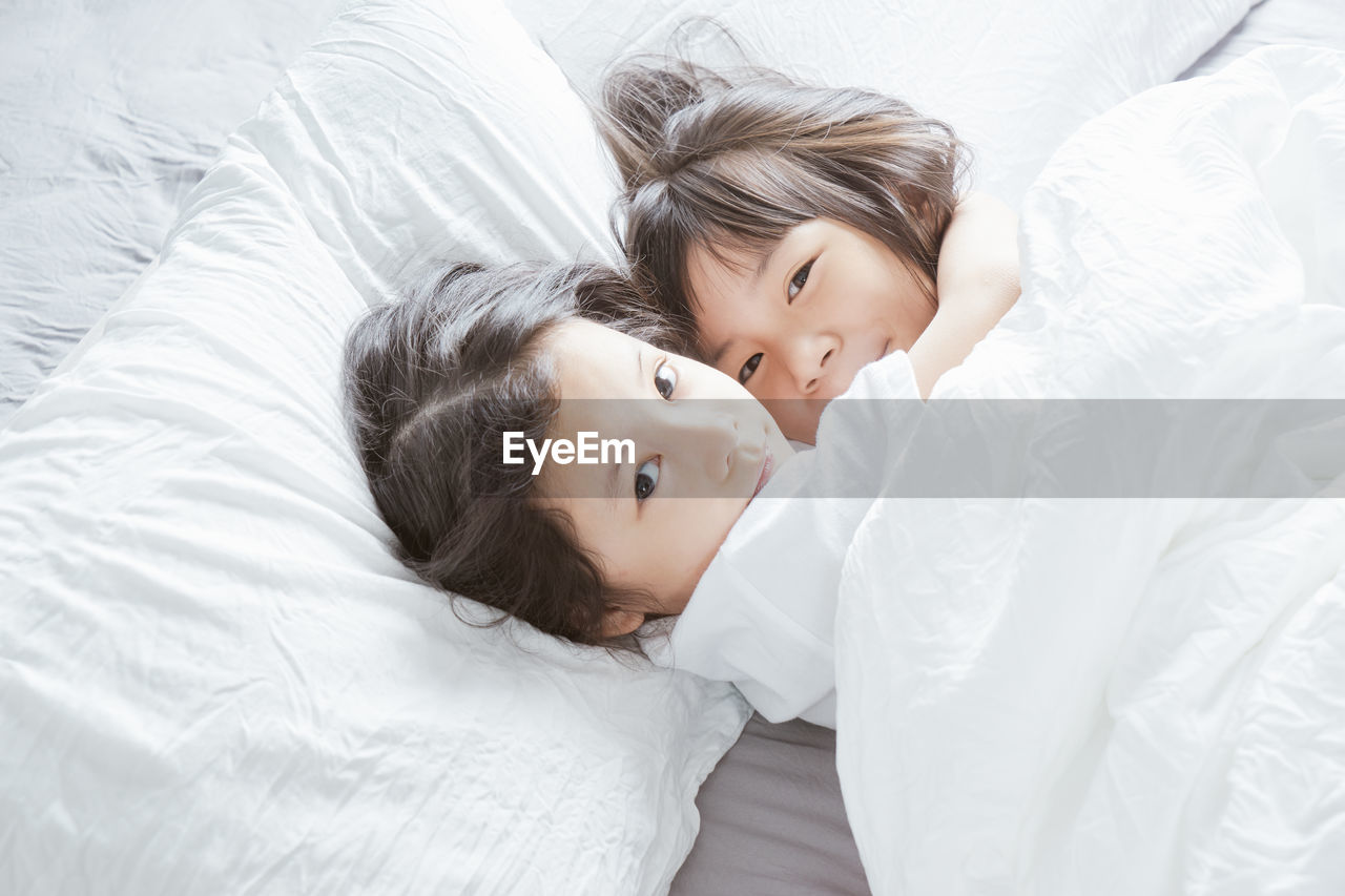 High angle portrait of siblings lying on bed