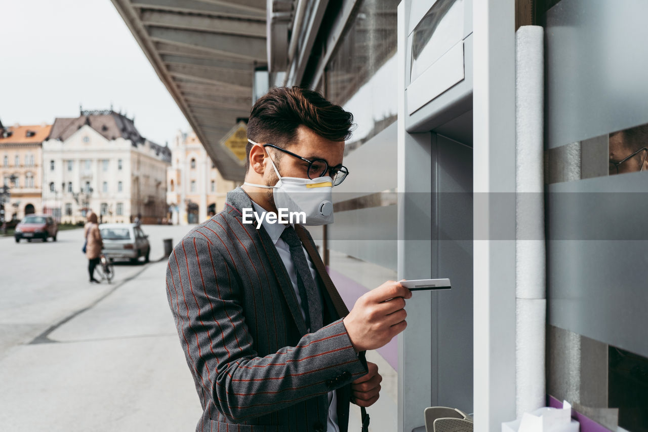 Business man with protective face mask using street atm machine.