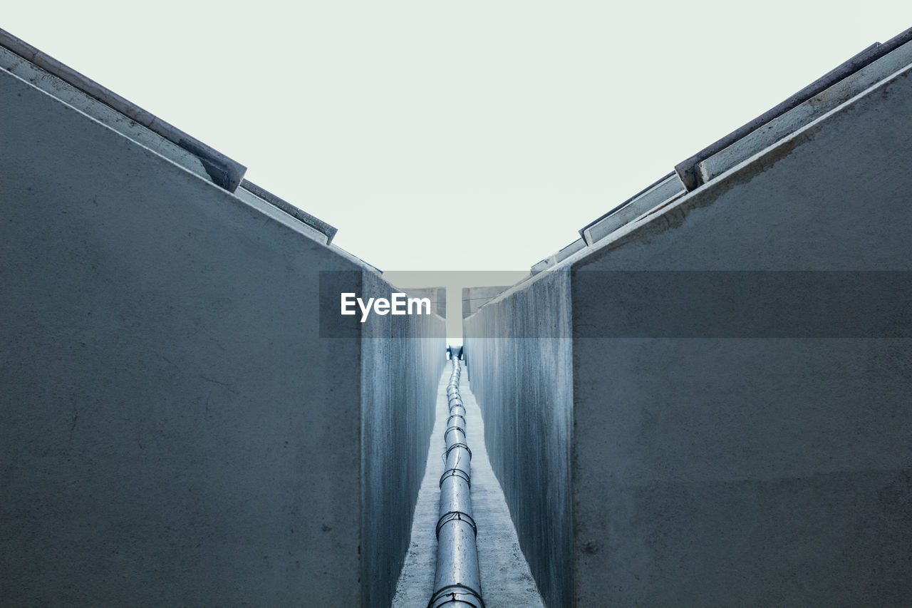 Water pipe amidst wall against clear sky