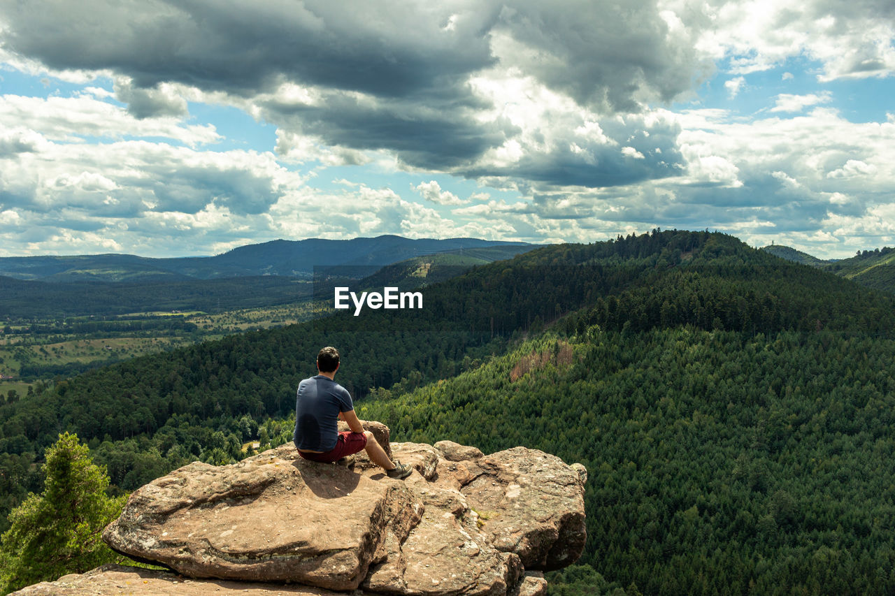 Rear view of man sitting on rock against sky