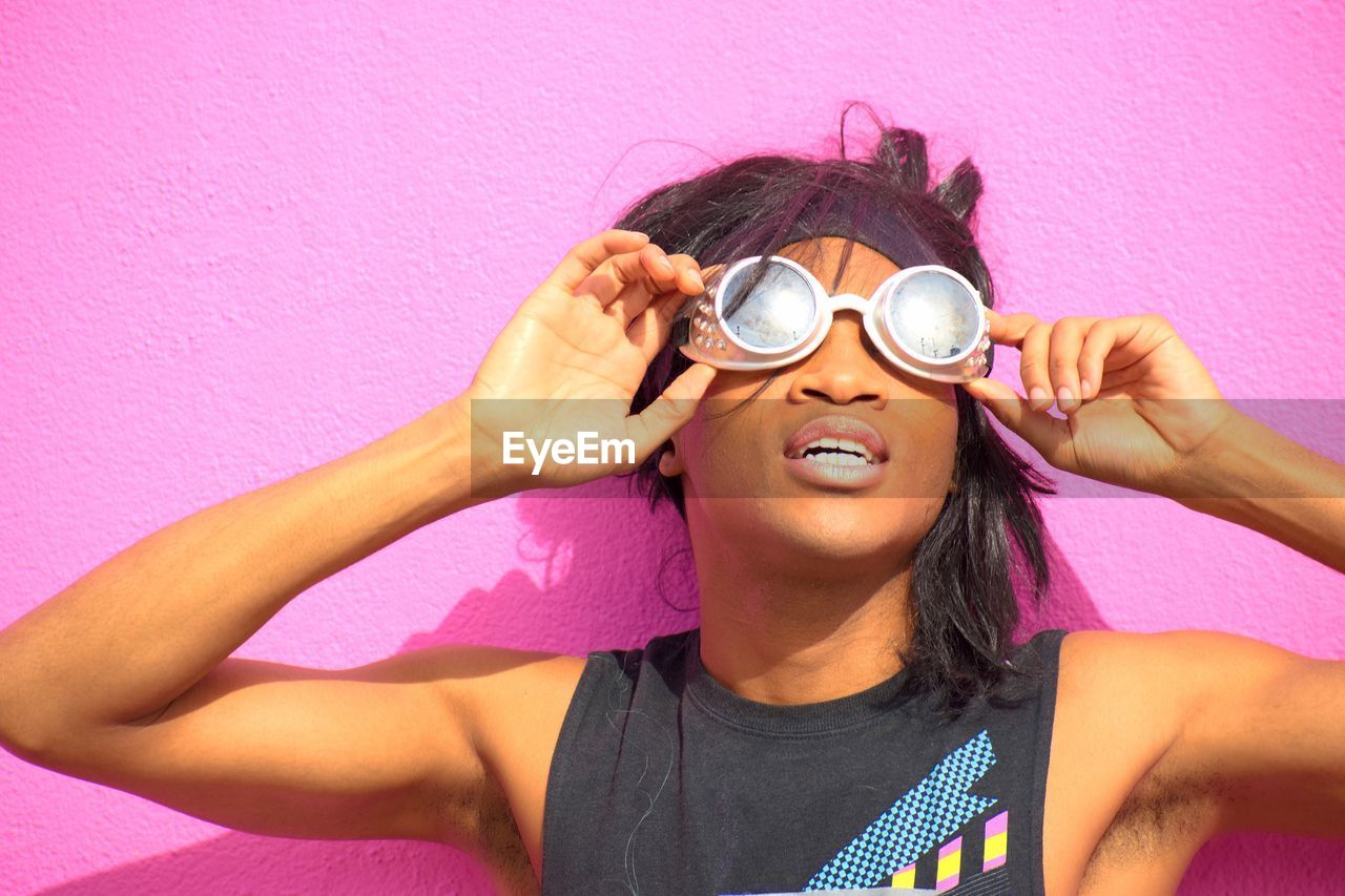 PORTRAIT OF YOUNG WOMAN HOLDING SUNGLASSES AGAINST PINK WALL AGAINST GRAY BACKGROUND